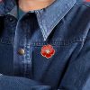 A red poppy lapel pin with intricate petal detailing, symbolizing pride. The pin can be worn on a lapel, hat, tie, or as a brooch. It represents remembrance and support, often associated with veterans.